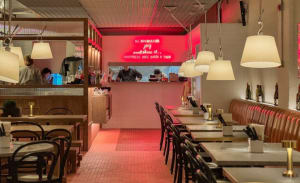 A warm and inviting restaurant interior with red accents, pink and white tiles, and dining tables with chairs and bottles