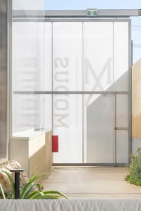 A modern building with a glass wall featuring letters and a metal facade with clear glass panels, set in a contemporary urban environment