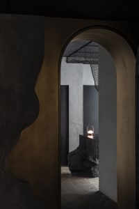 Modern entrance with concrete walls, black pillars, and a gold-framed doorway, illuminated by a nearby light source