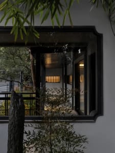 Asian-style house with a large window, black door, white wall, potted plants, and a bench in a well-lit room
