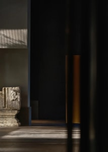 A stone statue on a pedestal in a museum-like space with a neutral color palette and subtle lighting