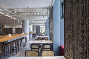 A spacious restaurant with multiple dining tables and chairs, featuring a mix of wood and tile flooring, white and grey walls, and a modern atmosphere