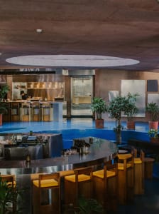 Modern restaurant interior with a circular bar, wood accents, metal elements, and potted plants, creating an inviting and comfortable atmosphere