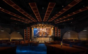 A lively bar with a stage in the center, surrounded by chairs and a dining table, creating a social gathering atmosphere