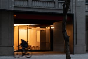 A bright and welcoming office space with natural light pouring in through a large window, featuring chairs and a bicycle in the foreground