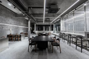 Open office space with a large black dining table, concrete walls and flooring, and multiple chairs and benches
