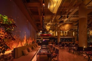 A modern restaurant dining area with multiple tables, couches, and artwork on the walls, featuring a warm and inviting atmosphere