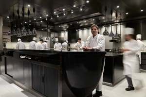 A bustling commercial kitchen with a black countertop island, multiple appliances, and several people working together