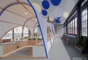 Open restaurant interior with multiple tables, chairs, potted plants, and round balls hanging from the ceiling