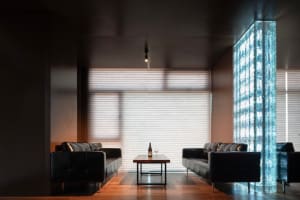 A modern living room with two black leather couches, chairs, a dining table, and a bottle on a table, surrounded by large windows