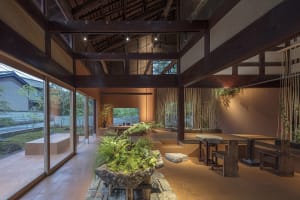 Cozy open space with wooden beams, stone floor, dining table, potted plants, and dim lighting