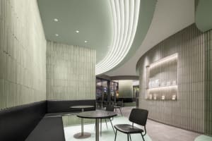 A modern restaurant interior with a green hue, featuring a large dining table and smaller table, multiple chairs, and warm lighting