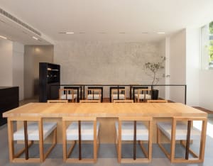 Open modern kitchen and dining space with wooden flooring and walls, featuring a large wooden dining table and two smaller tables with various items on them