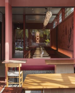 A modern restaurant interior with a long dining table, pink walls, and comfortable seating for guests