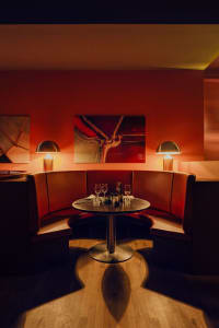 Cozy dining area with a round table, wine glasses, and bottles, surrounded by red-hued walls
