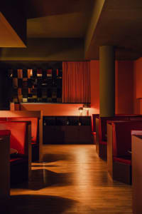 An inviting restaurant with red walls, wooden floors, and chairs scattered throughout the dining area, with bottles and a pleasant atmosphere