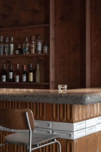 A cozy bar area with a counter featuring bottles of alcohol, wine glasses, and cups, surrounded by chairs in a social space