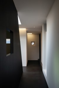 Narrow hallway with a black door and two windows on a white wall, creating a somewhat dark atmosphere