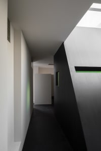 Narrow hallway with a black door, a white wall, and concrete walls, featuring an open and closed door