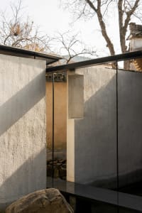 A stone building with a concrete wall featuring a glass panel and two windows, creating a calm and serene atmosphere with warm sunlight