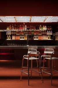A well-stocked bar with a long orange countertop, surrounded by chairs and a selection of bottles on display