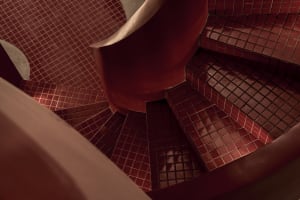 A well-lit staircase with red brick walls, wooden steps, and a metal railing, creating a warm and cozy atmosphere