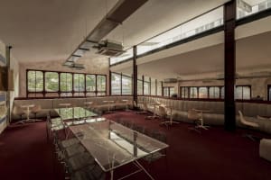 A spacious restaurant interior with a large dining table, red walls, and natural light from windows
