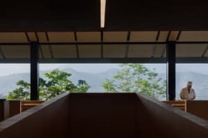 A house with a wooden facade and a large window overlooking a mountain range, creating a serene atmosphere