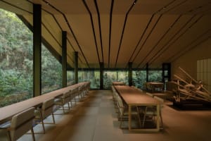 A spacious dining area with a long wooden table and chairs, illuminated by natural light through windows, creating a warm and inviting atmosphere