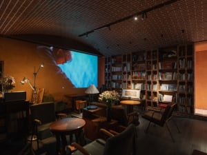 Cozy living space with a bookshelf, dining table, chairs, couch, and TV, featuring two people and a warm atmosphere