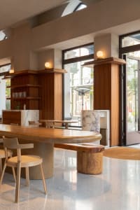 Well-lit restaurant interior with wooden tables, marble countertops, and a large window allowing natural light to enter