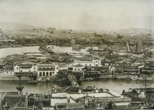A black and white photo of a historic city with a mix of architectural styles, including Chinese architecture, featuring stone buildings and boats in the water