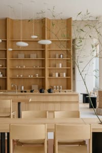 Cozy modern restaurant interior with wooden floors and walls, featuring a dining area with chairs and a large bookshelf in the background