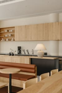 A modern kitchen and dining area with wooden floors and cabinets, featuring a dining table, couches, a chair, and kitchen appliances