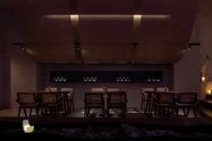 Empty restaurant with wooden tables and chairs, wine bottles, and a quiet, inviting atmosphere