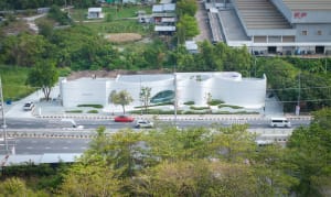 Modern museum building with a white exterior, surrounded by parked cars and a red vehicle in the center of the scene