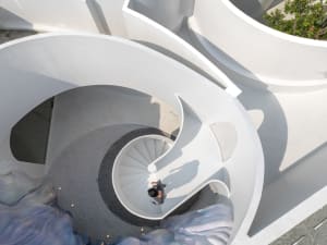 A rendered interior scene featuring a white spiral staircase in a modern building, with a clean and elegant atmosphere