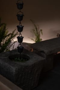 A calm indoor space with a stone bench, potted plants, and vases, surrounded by a serene atmosphere