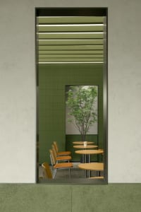 A restaurant interior with green walls, dining tables, chairs, and a potted plant, creating a cozy atmosphere for guests