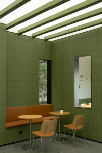 A calm and inviting restaurant interior with green walls, two tables, and three chairs, with two cups on the tables