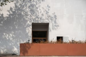 A traditional house with a red brick wall and two windows, one larger than the other, with a textured brick appearance and natural daylight