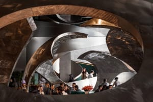 A modern hotel lobby with a circular design element, metal and glass materials, and soft diffused lighting, featuring several people in the space