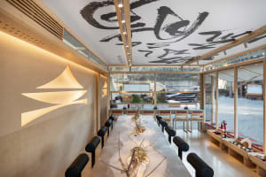 A dining area with a long wooden table surrounded by chairs, potted plants, and Chinese character artwork on the walls, creating a warm and inviting atmosphere