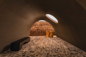 A cozy stone-walled room with a circular window, a bench, and scattered stones, featuring a warm and inviting atmosphere