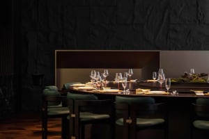 Dining area with a long wooden table set with wine glasses, surrounded by multiple chairs in a sophisticated and inviting environment