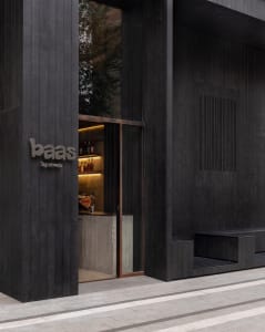 Modern bar entrance with a black doorway, a sign reading BAAS, and a well-stocked bar area with bottles on surfaces