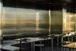 A modern restaurant with several dining tables and chairs, featuring reflective surfaces and a sophisticated atmosphere