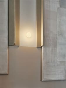 A modern interior space with a minimalist aesthetic, featuring a white-painted room with a wall-mounted light fixture and a round light source creating a warm atmosphere