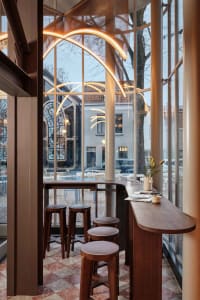 A cozy dining or socializing area with a wooden bar counter and chairs, featuring a potted plant and a warm atmosphere