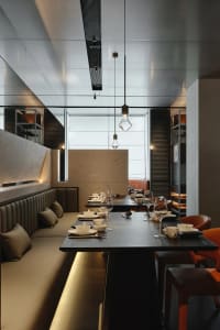 A dimly lit restaurant interior with modern furniture and table settings, featuring wine glasses, cups, and vases, creating a sophisticated atmosphere